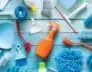 Various cleaning supplies including brushes, scrubbers, sponges, a spray bottle, dustpans, and gloves arranged on a blue wooden surface. The items are colorful with shades of blue, green, orange, red, and yellow—ideal for any Residential Cleaning DuPage County tasks.